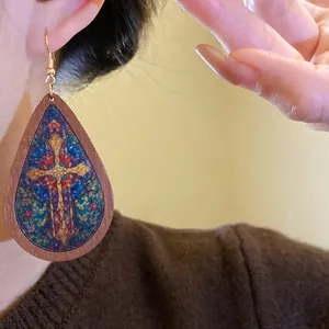 Close-up of Bohemian teardrop earrings with wood frame and stained glass cross print