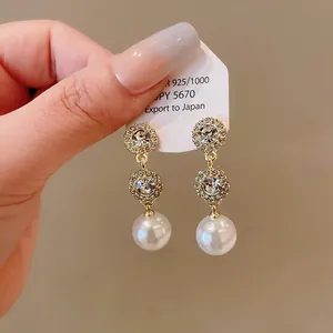Detail view of gold-tone pearl earrings with sparkling crystal accents and round drops.