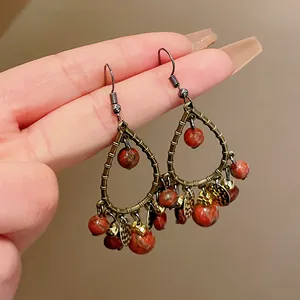 Close-up of vintage bronze teardrop earrings with red stone beads and metallic charms
