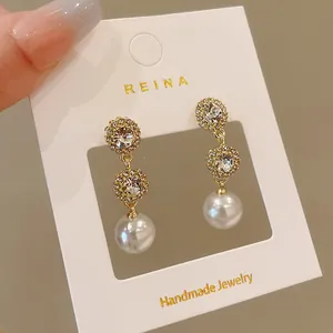 Close-up detail of elegant gold-toned earrings featuring rhinestones and white pearls on a display card