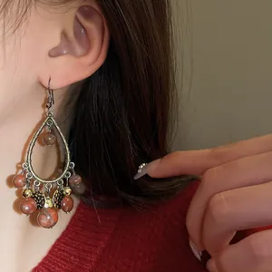 Detailed close-up of retro teardrop tassel earrings with reddish stone beads worn by model