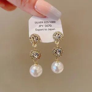 Detail view of rhinestone-encrusted round pearl drop earrings with silver pins