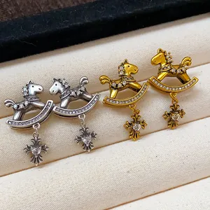 Detailed view of silver and gold rocking horse earrings with cross charms and zircons.