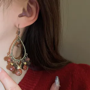 Close-up of vintage teardrop tassel earrings with reddish-brown beads on an Asian model.
