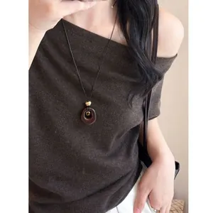 Close-up detail of a minimalist oval resin pendant necklace worn on brown knitwear