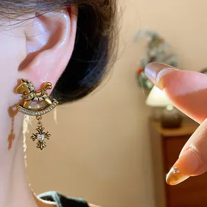 Close-up of golden rocking horse and cross charm earring with sparkling zircons