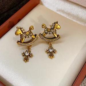 Detailed view of vintage gold rocking horse earrings with cross pendants and zircons.