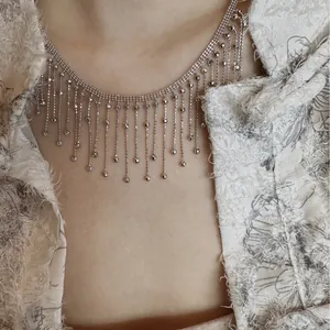 Gros plan d'un collier à pampilles géométriques porté avec une veste en tweed