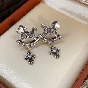 Detail view of rocking horse earrings with heart-centered cross charms and zircons