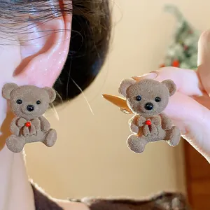 Close-up of brown flocked teddy bear earrings with soft texture and red bow detail