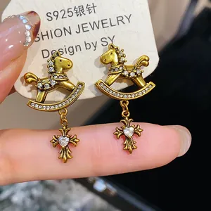 Close-up of vintage gold rocking horse earrings with cross zircon pendants on card