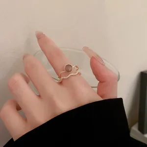 Vue détaillée d'une élégante bague dorée à vagues avec zircon et bague ronde au doigt