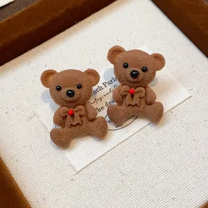 Close-up detail of cute brown flocked teddy bear stud earrings with red accents.