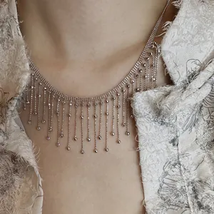 Détail d'un collier à franges argenté sur un vêtement de luxe en tissu crème texturé