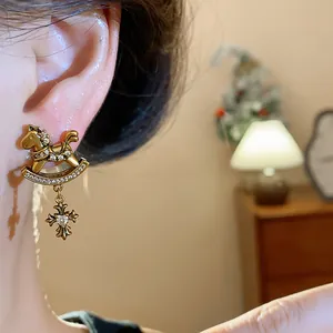 Close-up detail of vintage gold rocking horse earring with dangling zircon heart cross