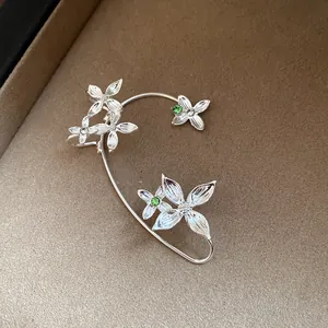 Gros plan détaillé d'un élégant ear cuff fleur en argent avec des strass verts brillants