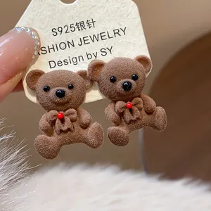 Macro detail of brown flocked teddy bear earrings with red bow on silver needle.