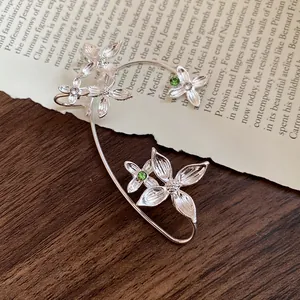 Détail élégant d'un ear cuff fleuri en argent avec cristaux verts sur fond de papier