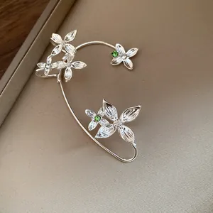 Détail d'un ear cuff fleuri argenté avec des strass étincelants transparents et verts.