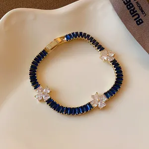 Elegantes goldfarbenes Armband mit blauen Steinen und weißen Zirkonblüten in Nahaufnahme