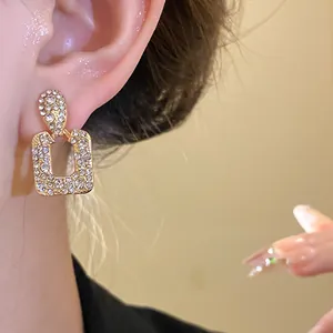 Close-up detail of elegant gold geometric drop earrings with sparkling rhinestone inlay