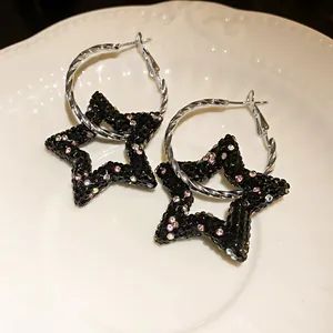 Dettaglio di orecchini a cerchio con stella di strass neri su un piatto bianco ceramica