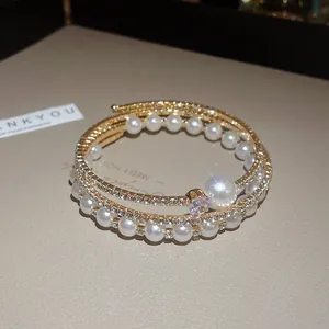 Primo piano di un elegante bracciale dorato multistrato con perle bianche e strass scintillanti.