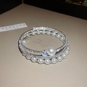 Dettaglio ravvicinato di un bracciale multistrato con perle eleganti e strass scintillanti.