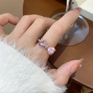 Primo piano di un anello a fiocco con cuore rosa e pietre di zircone al dito.