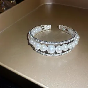 Dettaglio di un bracciale rigido multistrato aperto con strass e perle bianche