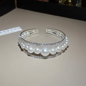 Dettaglio di un bracciale a polsino multistrato di lusso con strass scintillanti e perle bianche