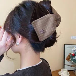 Détail d'une grande pince à cheveux avec nœud en tissu marron rayé et bouton décoratif