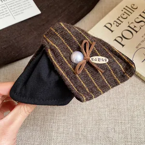 Détail d'une pince à cheveux de luxe en tissu rayé marron ornée d'une perle et d'un nœud