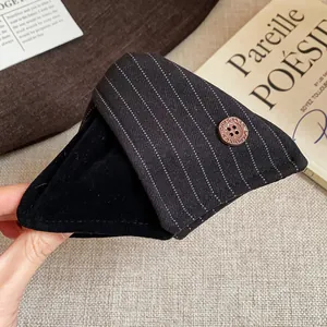 Gros plan d'une pince à cheveux en tissu rayé avec un bouton marron vintage.