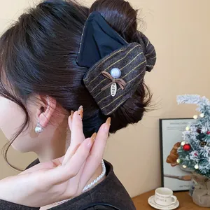 Gros plan d'une grande pince à cheveux nœud en tissu avec perle et rayures dorées.