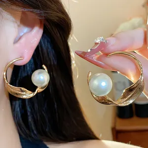 Detalle de pendiente de aro metálico dorado con gran perla blanca en la oreja