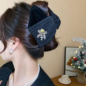 Détail d'une grande pince à cheveux en tissu noir élégamment portée sur des cheveux bruns.