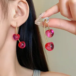 Korean style sweet red resin cherry drop earrings with gold stems shown on model's ear
