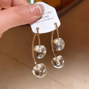 Detail view of clear cherry-shaped resin drop earrings with gold-tone curved bars