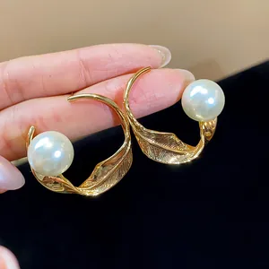 Primer plano de pendientes de aro dorados en forma de hoja con perlas blancas grandes.
