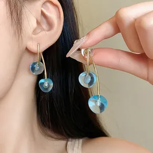 Detail view of blue resin cherry drop earrings with elegant golden stems and silver pins.