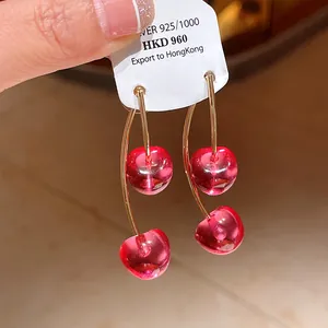 Macro detail of red resin cherry earrings with gold stems and S925 silver needles