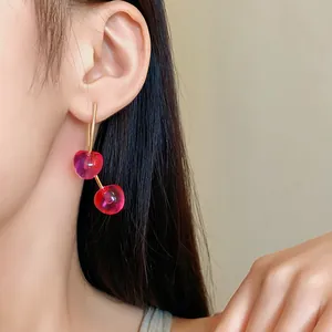Close-up detail of a model wearing minimalist translucent pink cherry resin earrings with gold hooks