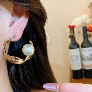 Primer plano de un elegante pendiente de aro dorado retorcido con perla puesto en la oreja