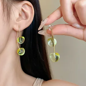 Close-up of green cherry resin earrings showing translucent texture and gold finish.
