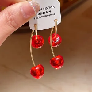Close-up detail showing the glossy red resin cherry earrings with gold-plated hooks