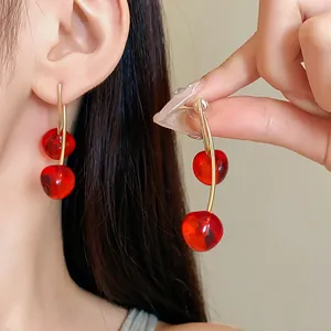 Detailed close-up view of vibrant red cherry resin drop earrings worn on a model ear