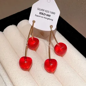 Close-up detail of red cherry resin earrings with silver needles on display card
