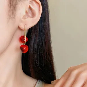 Elegant red cherry resin drop earrings with gold hooks shown on an Asian model