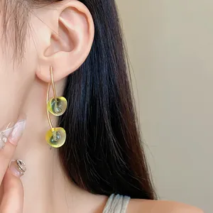 Detail view of yellow resin cherry drop earrings on a model for a chic summer look.
